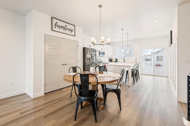 dining space with sink, light hardwood / wood-style flooring, and a notable chandelier