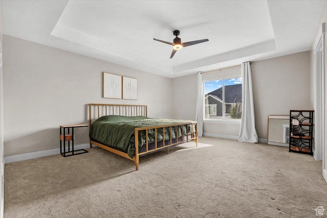 carpeted bedroom with a raised ceiling and ceiling fan