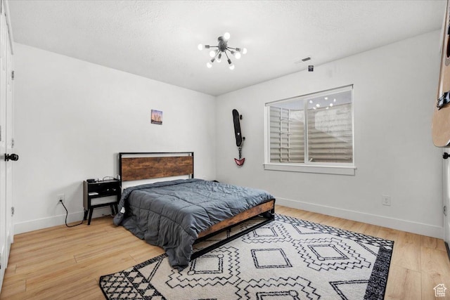 bedroom with light hardwood / wood-style floors, a chandelier, and a textured ceiling
