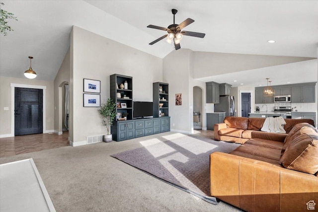 carpeted living room with ceiling fan, sink, and high vaulted ceiling