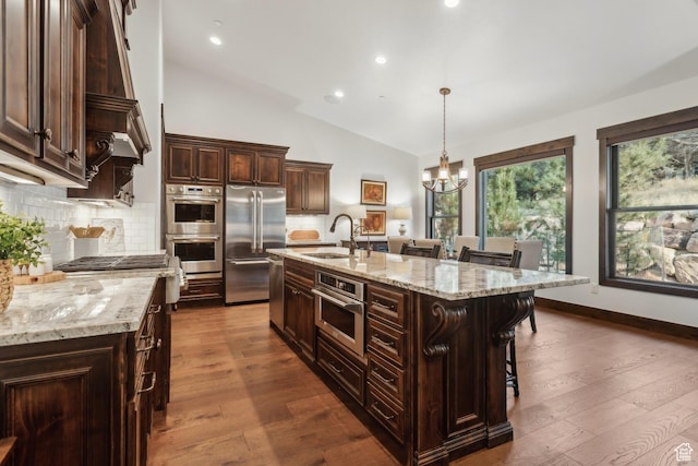 kitchen featuring pendant lighting, a breakfast bar, appliances with stainless steel finishes, light stone countertops, and an island with sink