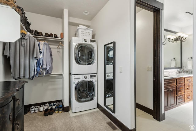 laundry area with stacked washer / drying machine, a notable chandelier, sink, and light tile patterned flooring