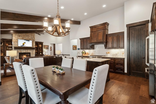 dining room featuring a stone fireplace, dark hardwood / wood-style floors, high vaulted ceiling, beamed ceiling, and sink