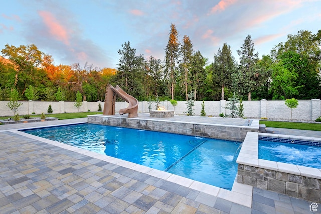 view of swimming pool featuring a fire pit, a water slide, a fenced backyard, and a patio area
