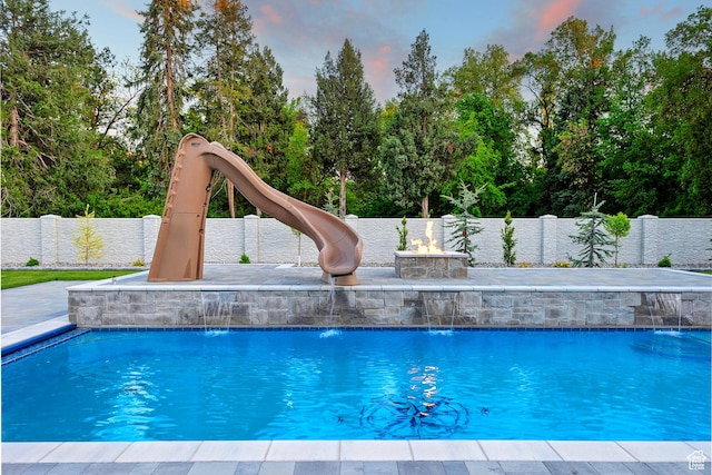 pool at dusk featuring a fenced in pool, a water slide, a fenced backyard, and a patio area