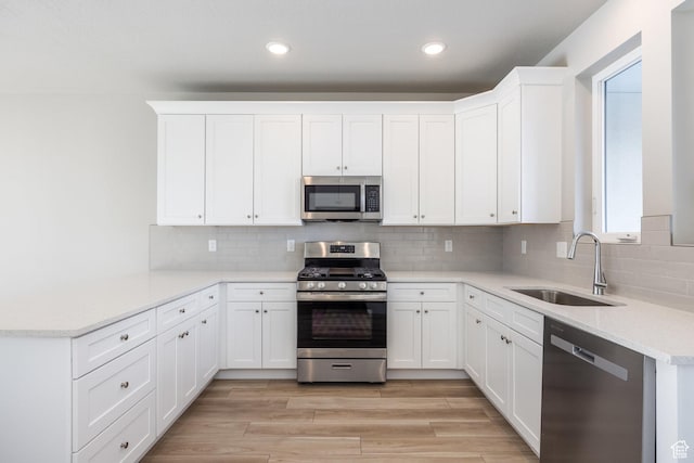 kitchen with sink, white cabinetry, light wood-type flooring, stainless steel appliances, and decorative backsplash