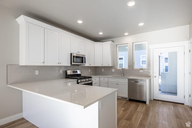 kitchen featuring appliances with stainless steel finishes, sink, white cabinets, light hardwood / wood-style floors, and kitchen peninsula