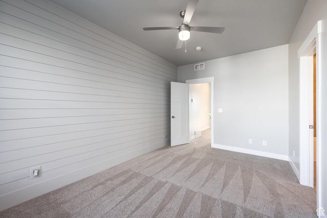 unfurnished bedroom with ceiling fan, light carpet, and wooden walls