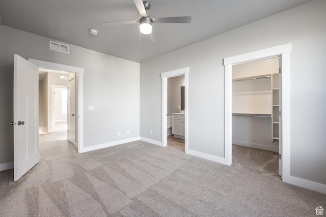 unfurnished bedroom featuring a walk in closet, light carpet, connected bathroom, and a closet