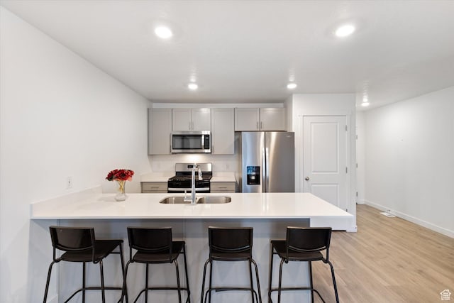 kitchen with appliances with stainless steel finishes, gray cabinetry, a breakfast bar area, and kitchen peninsula