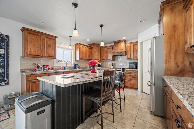 kitchen featuring custom exhaust hood, light stone counters, decorative light fixtures, a center island, and appliances with stainless steel finishes