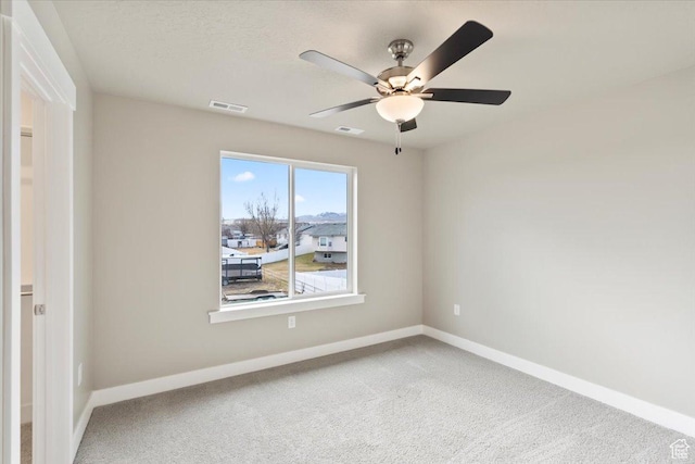 carpeted spare room with visible vents, baseboards, and a ceiling fan