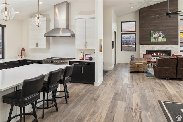 3450 N 1930 E, North Logan, UT 84341 - kitchen featuring a breakfast bar, white cabinetry, hanging light fixtures, stainless steel gas cooktop, and wall chimney exhaust hood