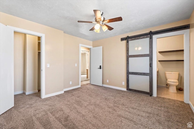 unfurnished bedroom featuring carpet flooring, a barn door, baseboards, ensuite bathroom, and a textured ceiling