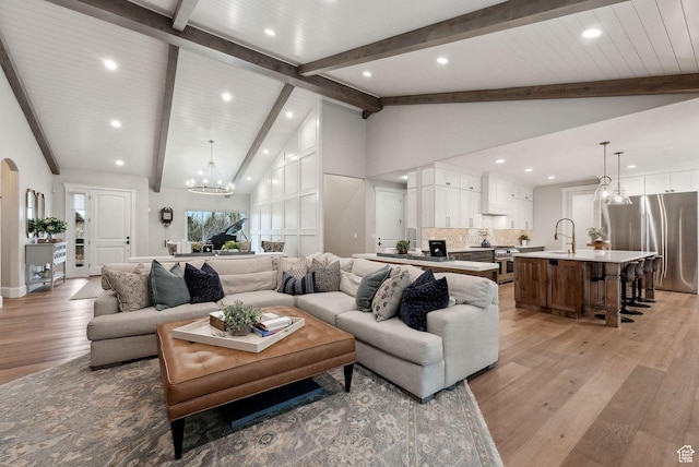 living room with an inviting chandelier, high vaulted ceiling, light wood-style floors, and beamed ceiling