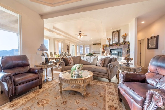 living room with ceiling fan, a tray ceiling, and a fireplace
