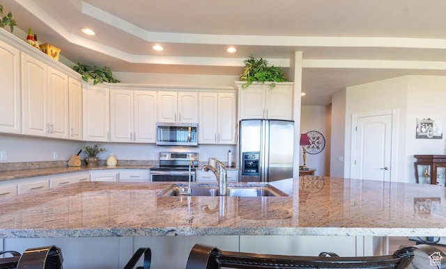 kitchen featuring sink, a breakfast bar area, appliances with stainless steel finishes, light stone countertops, and white cabinets