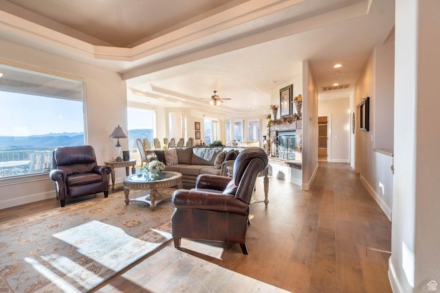living room featuring ceiling fan, a mountain view, light hardwood / wood-style floors, and a tray ceiling