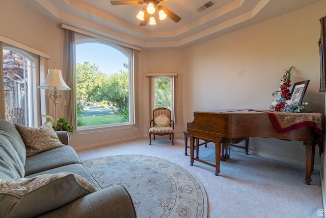 living area featuring ceiling fan, light colored carpet, and a tray ceiling