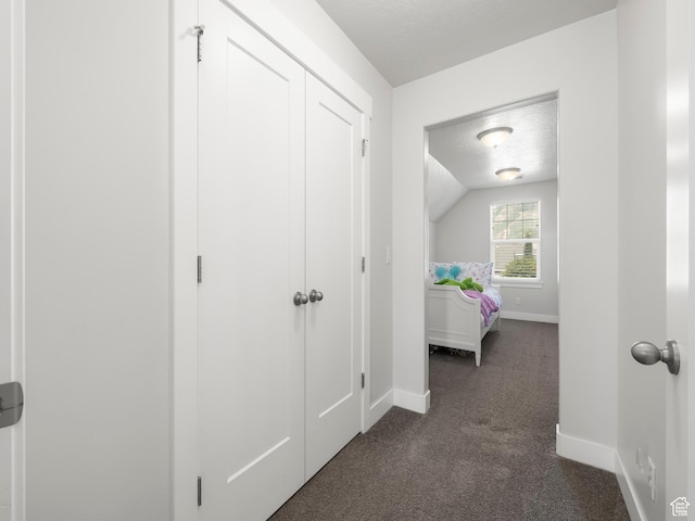 interior space featuring vaulted ceiling, dark carpet, a textured ceiling, and baseboards