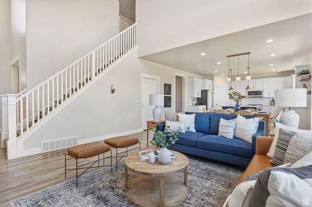 living area with baseboards, visible vents, a towering ceiling, stairway, and light wood-style floors