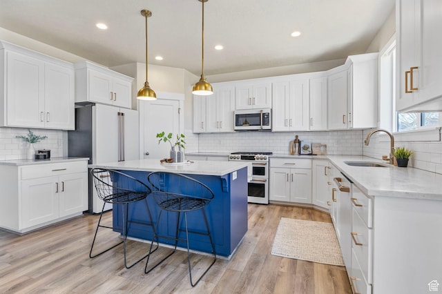 kitchen with appliances with stainless steel finishes, a sink, light wood finished floors, and a kitchen island