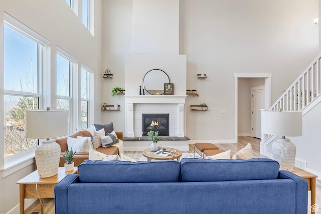 living area with a wealth of natural light, a brick fireplace, baseboards, and wood finished floors