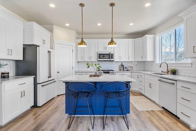 kitchen featuring light wood finished floors, white appliances, a kitchen island, and a sink