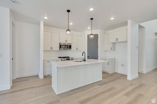 kitchen with an island with sink, baseboards, stainless steel appliances, and a sink
