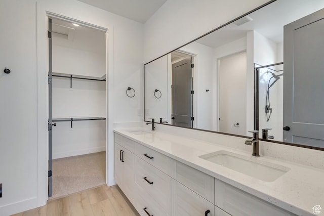 full bath featuring wood finished floors, a sink, a shower stall, and double vanity