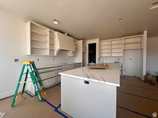 1589 S 4000 W Unit 12, Hurricane, UT 84737 - kitchen with open shelves, custom range hood, an island with sink, baseboards, and light stone countertops