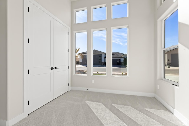 unfurnished bedroom with a closet, baseboards, light colored carpet, and a high ceiling