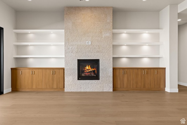 unfurnished living room with a tiled fireplace, built in shelves, and light wood-style floors