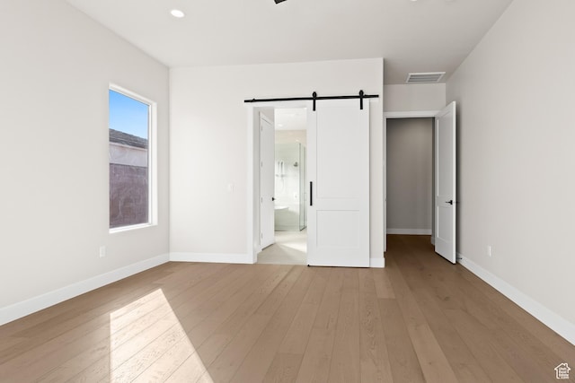 unfurnished bedroom with baseboards, a barn door, wood-type flooring, and visible vents