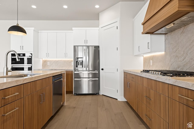kitchen featuring custom range hood, appliances with stainless steel finishes, light wood-style floors, white cabinets, and a sink