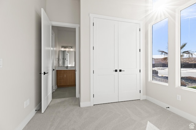 unfurnished bedroom with a closet, light colored carpet, and baseboards