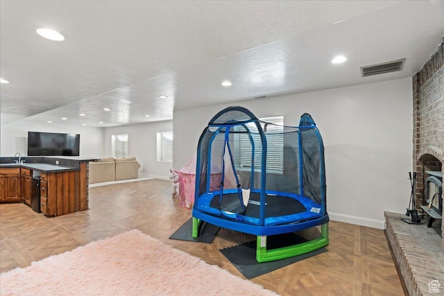 playroom with sink, a textured ceiling, a fireplace, and light parquet floors