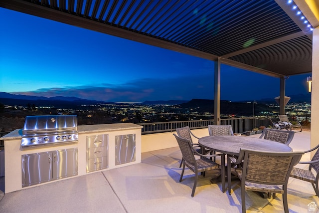 patio terrace at dusk with a grill, a mountain view, and an outdoor kitchen