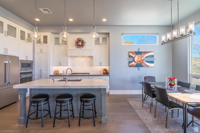 kitchen featuring sink, a center island with sink, appliances with stainless steel finishes, light stone countertops, and white cabinets