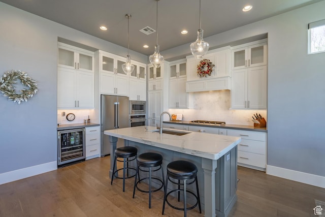 kitchen with sink, a kitchen island with sink, stainless steel appliances, wine cooler, and white cabinets