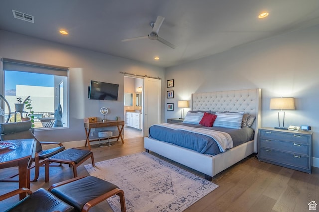 bedroom with light hardwood / wood-style flooring, a barn door, ceiling fan, and ensuite bathroom
