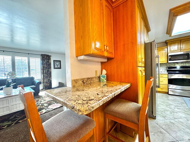 500 W Clark St S, Grantsville, UT 84029 - kitchen with light tile patterned floors, brown cabinets, stainless steel appliances, and a kitchen bar