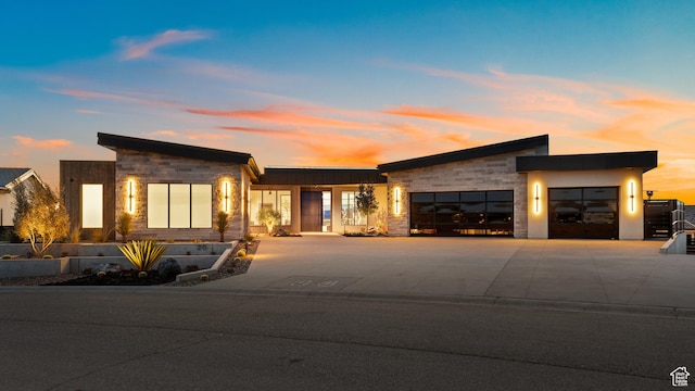 modern home with stone siding, driveway, and an attached garage
