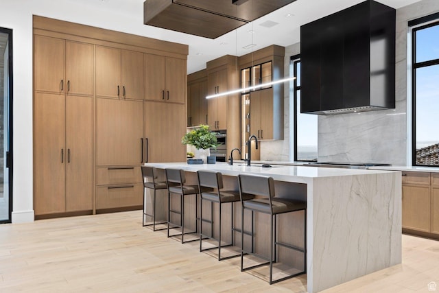 20 N Cliffside Dr, Washington, UT 84780 - kitchen with decorative backsplash, an island with sink, light wood-style flooring, extractor fan, and a kitchen bar