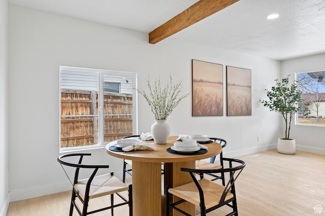 dining area featuring beamed ceiling, a textured ceiling, and light wood-type flooring