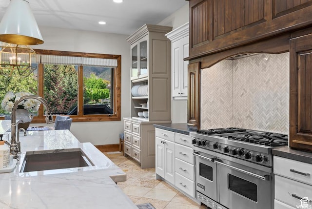 kitchen featuring sink, dark stone countertops, white cabinets, backsplash, and range with two ovens