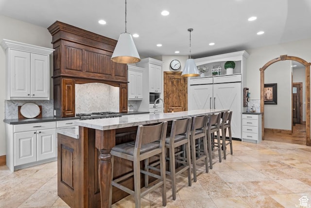 kitchen featuring white cabinets, decorative light fixtures, a large island with sink, and a kitchen bar