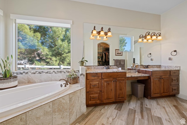 bathroom featuring vanity, a relaxing tiled tub, a wealth of natural light, and wood-type flooring