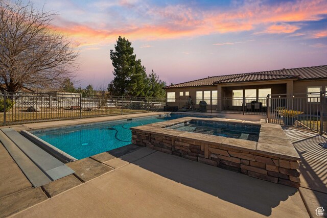 pool at dusk featuring a patio and an in ground hot tub
