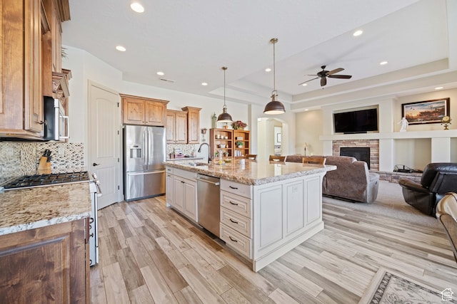 kitchen with light stone counters, decorative light fixtures, a raised ceiling, an island with sink, and stainless steel appliances